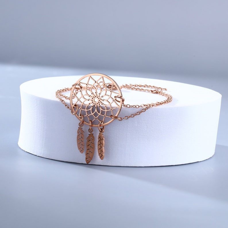 May include: A rose gold dreamcatcher bracelet with a delicate chain and three feather charms.