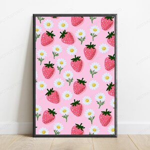 May include: A rectangular framed wall art print featuring a repeating pattern of red strawberries with green stems and white daisies with yellow centers on a solid light pink background. The frame is thin and black with a clean, simple edge.