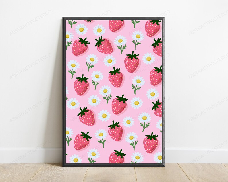 May include: A rectangular framed wall art print featuring a repeating pattern of red strawberries with green stems and white daisies with yellow centers on a solid light pink background. The frame is thin and black with a clean, simple edge.
