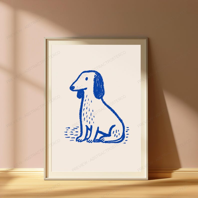 K&ouml;nnte beinhalten: Ein gerahmter Wandkunstdruck mit einer einfachen, handgezeichneten Illustration eines sitzenden Hundes in tiefblauer Tinte auf hellcremefarbenem Hintergrund. Der Hund hat lange Ohren, ein strukturiertes Fellmuster und ist mittig platziert.