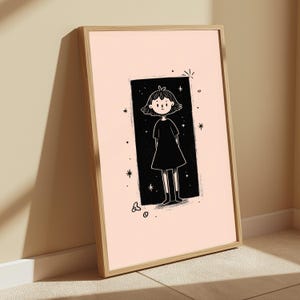 May include: A framed wall art print featuring a light peach background and a central black rectangular panel. Inside the panel is a line-art illustration of a person with short hair wearing a dress, surrounded by small white star and dot accents.