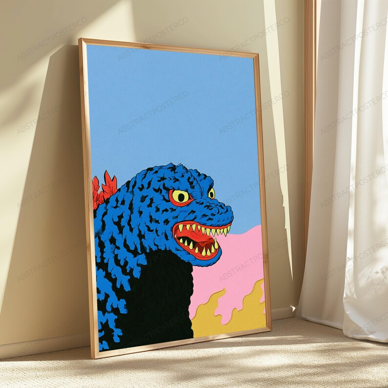 May include: A framed vertical poster featuring a stylised illustration of a blue monster with yellow eyes and sharp teeth. The creature has red dorsal fins, a black chest, and is set against a light blue sky with pink and yellow abstract shapes.