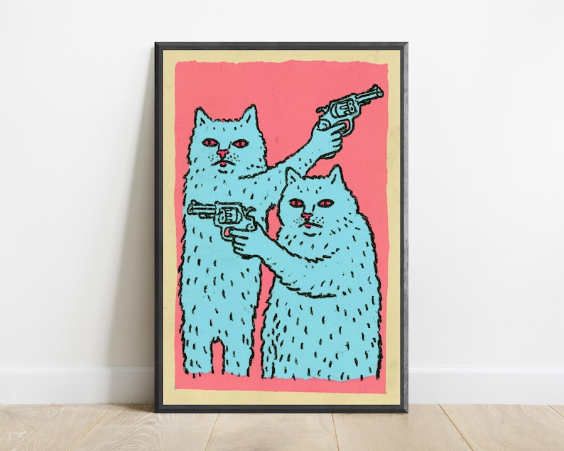 May include: A framed wall art print featuring two light blue cats with red eyes against a solid pink background. Each cat is holding a dark-coloured revolver, with one cat pointing its weapon upward and the other pointing its weapon forward.