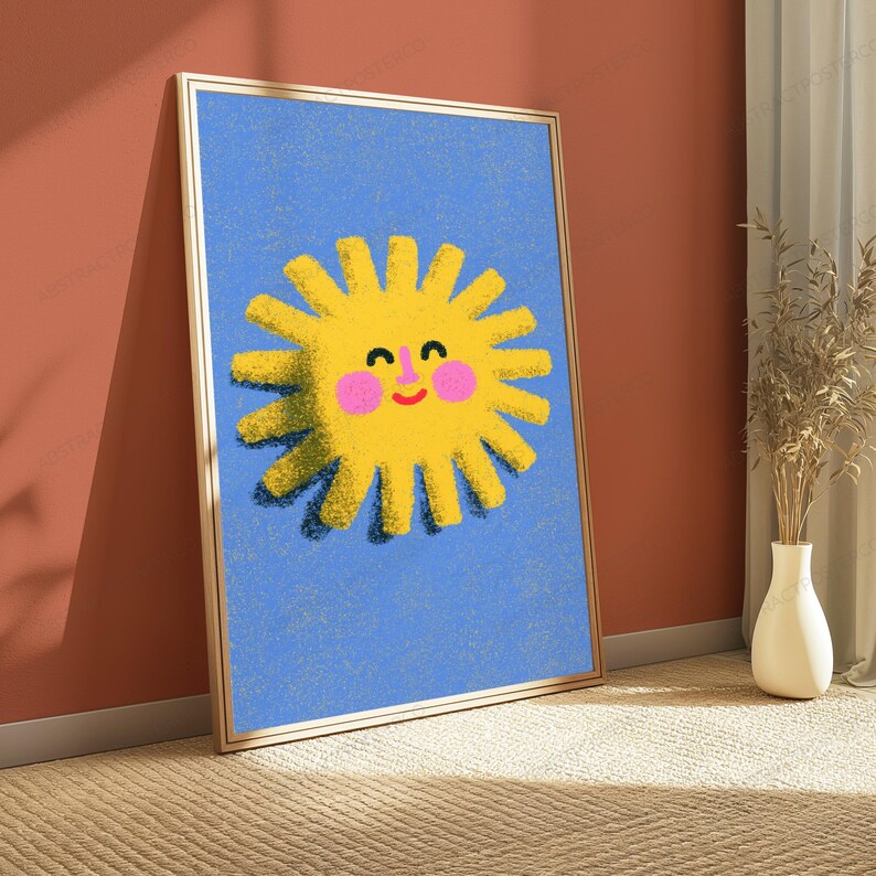 May include: A framed vertical wall art print featuring a bright yellow sun with a smiling face, pink cheeks, and a textured appearance set against a solid blue background. The sun has numerous rays extending outward and a dark shadow effect.