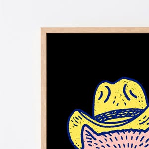 Puede incluir: Una impresi&oacute;n de arte mural enmarcada que presenta una ilustraci&oacute;n estilizada de un gato con un sombrero de vaquero amarillo con un contorno azul oscuro. El gato tiene pelaje rosa claro con marcas texturizadas rosa oscuro sobre fondo negro.