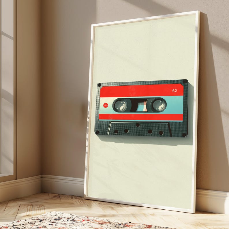May include: A framed vertical wall art print featuring a centered illustration of a cassette tape. The tape has a black outer shell, a bright red upper section, and a light blue lower section. The number 62 is printed in white on the red area.