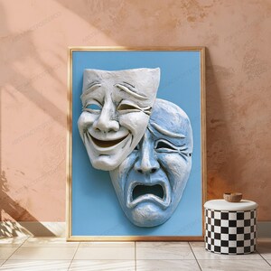 May include: A framed wall art print featuring two theatrical masks against a solid light blue background. The top mask is white with a smiling expression, while the partially overlapping bottom mask is light blue with a sad, crying expression.