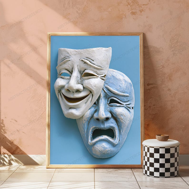 May include: A framed wall art print featuring two theatrical masks against a solid light blue background. The top mask is white with a smiling expression, while the partially overlapping bottom mask is light blue with a sad, crying expression.