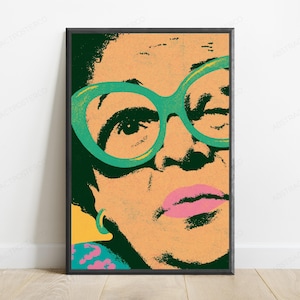 May include: A framed pop art style print featuring a close-up portrait of a person with dark hair, wearing large, bright green cat-eye glasses. The face is rendered in peach tones with dark green shadows, pink lips, and a small turquoise hoop earring.