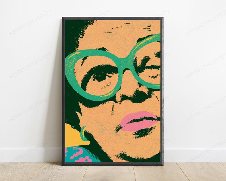 May include: A framed pop art style print featuring a close-up portrait of a person with dark hair, wearing large, bright green cat-eye glasses. The face is rendered in peach tones with dark green shadows, pink lips, and a small turquoise hoop earring.