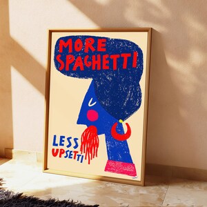 May include: A framed wall art print on a cream background featuring a blue stylized profile of a person with a large blue textured hairstyle. The text reads MORE SPAGHETTI! and LESS UPSETTI in red and blue. A red hoop earring and red spaghetti are visible.