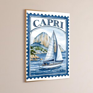 May include: A framed wall art print designed like a postage stamp featuring a watercolor illustration of a sailboat on blue water with a rocky mountain and coastal buildings in the background. The word CAPRI is printed in dark blue at the top.