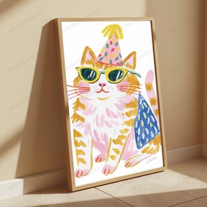 K&ouml;nnte beinhalten: Ein gerahmter Kunstdruck, der eine stilisierte orangefarbene getigerte Katze mit einem rosa Partyhut mit bunten Konfettipunkten und einer gelb umrandeten Sonnenbrille zeigt. Die Katze hat rosa Akzente im Fell und ein blaues Dreiecksmuster.