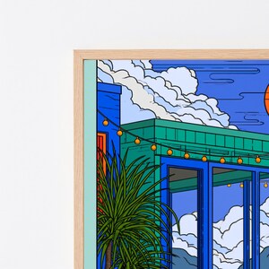 May include: A framed digital art print featuring a modern building with blue and teal walls, large glass windows, and a string of glowing yellow lights. A spiky green potted plant sits in the foreground under a bright blue sky with white clouds.