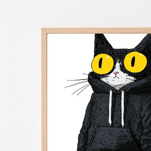 K&ouml;nnte beinhalten: Eine gerahmte Illustration einer schwarzen Katze mit gro&szlig;en, leuchtend gelben Augen und wei&szlig;er Schnauze, die einen schwarzen Kapuzenpullover mit wei&szlig;en Kordeln tr&auml;gt. Das Bild hat eine detaillierte, skizzenhafte Textur auf wei&szlig;em Grund.