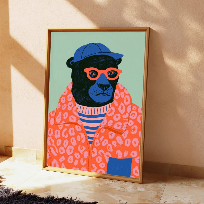 May include: A framed art print featuring a black panther wearing a blue baseball cap, bright orange glasses, a blue and white striped shirt, and an orange jacket with a pink leopard print pattern. The background is a solid light green color.