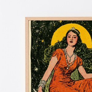 May include: A framed art print featuring a person with long dark hair wearing a tiara and an orange dress. The person is positioned against a dark green starry background with a large yellow circle behind their head. A multi-strand necklace is worn.