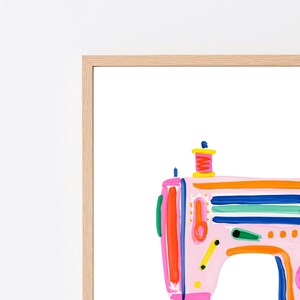 Pu&ograve; includere: Una stampa artistica da parete incorniciata che presenta un'illustrazione stilizzata e colorata di una macchina da cucire. La macchina &egrave; resa con tratti di vernice vivaci in rosa, arancione, blu, verde e giallo su uno sfondo bianco.