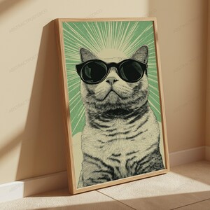 May include: A framed wall art print featuring a detailed illustration of a cat wearing large black sunglasses. The cat is centered against a light green background with radiating white sunburst lines extending from behind its head.