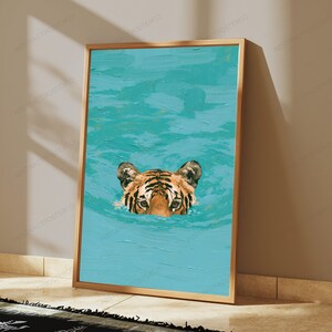 May include: A rectangular wall art print in a thin gold frame featuring an oil painting of a tiger head emerging from vibrant turquoise water. The tiger has orange fur with black stripes and is positioned in the lower centre of the composition.
