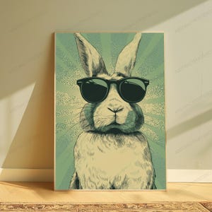 May include: A rectangular wall art print featuring a stylized illustration of a rabbit wearing black sunglasses. The rabbit is centered against a background of radiating light green and cream-colored sunburst lines with a textured dot pattern.