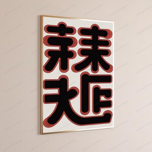 May include: A rectangular wall art print in a thin gold frame featuring four large, stylized black Chinese characters arranged in a two-by-two grid. Each character is outlined with a thick, textured red border against a cream background.