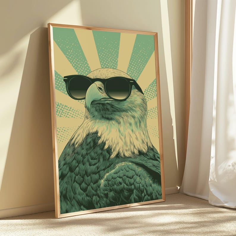 May include: A framed wall art print featuring a stylized illustration of a bald eagle wearing black sunglasses. The eagle is depicted against a background of radiating light green and pale yellow sunburst rays with a dotted texture pattern.