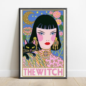 May include: A framed art print titled THE WITCH featuring a stylized illustration of a person with black hair, blue eyes, and red lips, wearing a pink floral top and ornate gold jewelry. A black cat sits on their shoulder against a blue background.
