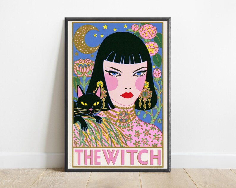 May include: A framed art print titled THE WITCH featuring a stylized illustration of a person with black hair, blue eyes, and red lips, wearing a pink floral top and ornate gold jewelry. A black cat sits on their shoulder against a blue background.