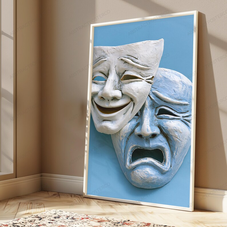 May include: A framed wall art print featuring two theatrical masks against a solid light blue background. One white mask displays a smiling expression, while the overlapping blue mask below it displays a sad, weeping expression with deep-set eyes.