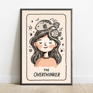 K&ouml;nnte beinhalten: Ein gerahmter Wandkunstdruck mit einer Strichzeichnung einer Person, auf deren Kopf zwei Fische ruhen. Der Hintergrund ist cremefarben mit kleinen Sternakzenten. Der Text am unteren Rand lautet THE OVERTHINKER in schwarzer Schrift.