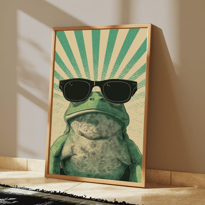 K&ouml;nnte beinhalten: Ein gerahmter vertikaler Wandkunstdruck, der einen gr&uuml;nen Frosch mit einer schwarzen Sonnenbrille zeigt. Der Hintergrund besteht aus einem hellbeigen und gr&uuml;nen Strahlenmuster mit einer gepunkteten Textur, wobei der Frosch mittig platziert ist.
