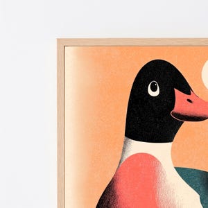 May include: A framed wall art print featuring a stylised illustration of a duck with a black head, a coral-coloured beak, and a white neck. The duck is set against a textured, light orange background with a partial white circular shape visible.
