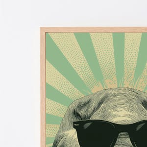 May include: A framed wall art print featuring a stylised illustration of an elephant wearing black sunglasses. The background consists of alternating light green and beige sunburst rays with a dotted texture pattern, all encased in a light wood frame.
