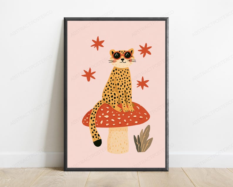 Op de afbeelding: Een ingelijste wandkunstprint met een gele luipaard met zwarte vlekken die een ronde oranje zonnebril draagt, zittend op een grote rode paddenstoel met witte stippen. De achtergrond is lichtroze met vier rode sterren en een kleine groene plant.
