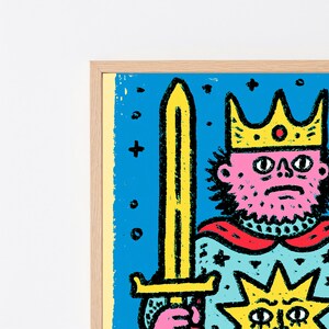May include: A framed art print featuring a pink-skinned character wearing a yellow crown and holding a long yellow sword. The background is bright blue with black star and dot accents. A stylized yellow sun icon is visible at the bottom right.