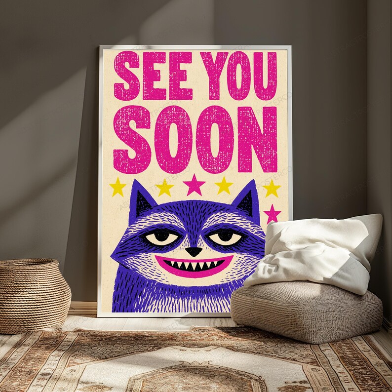 May include: A rectangular wall poster featuring the text SEE YOU SOON in bold pink letters at the top. Below the text is a stylized purple raccoon face with a wide grin showing sharp teeth, set against a cream background with small yellow and pink stars.