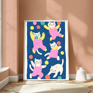 May include: A framed vertical art print featuring five white cats wearing pink overalls on a textured dark blue background. The cats are depicted in various playful poses, surrounded by scattered colorful circles in yellow, orange, pink, and teal.