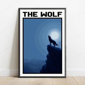 May include: A framed rectangular wall art print featuring a dark blue monochromatic landscape with a wolf standing on a cliff edge howling at a full moon. The text THE WOLF is printed in a bold black pixelated font at the top of the poster.