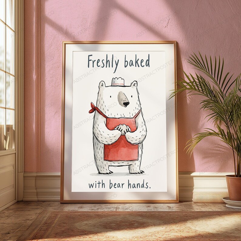 Puede incluir: Una l&aacute;mina enmarcada que muestra un oso blanco con un delantal rojo y un peque&ntilde;o gorro de chef. El oso est&aacute; de pie con las patas juntas. El texto "Freshly baked" aparece arriba y "with bear hands." est&aacute; impreso en la parte inferior.