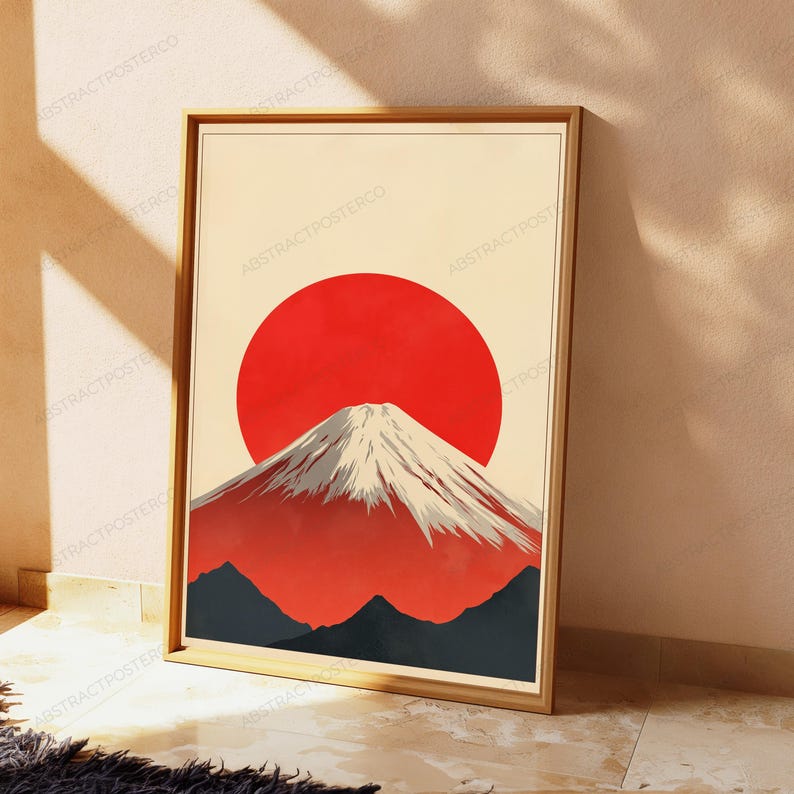 May include: A framed vertical wall art print featuring a stylized illustration of a snow-capped mountain peak centered in front of a large, solid red circular sun against a cream-colored background, with dark gray mountain silhouettes at the base.