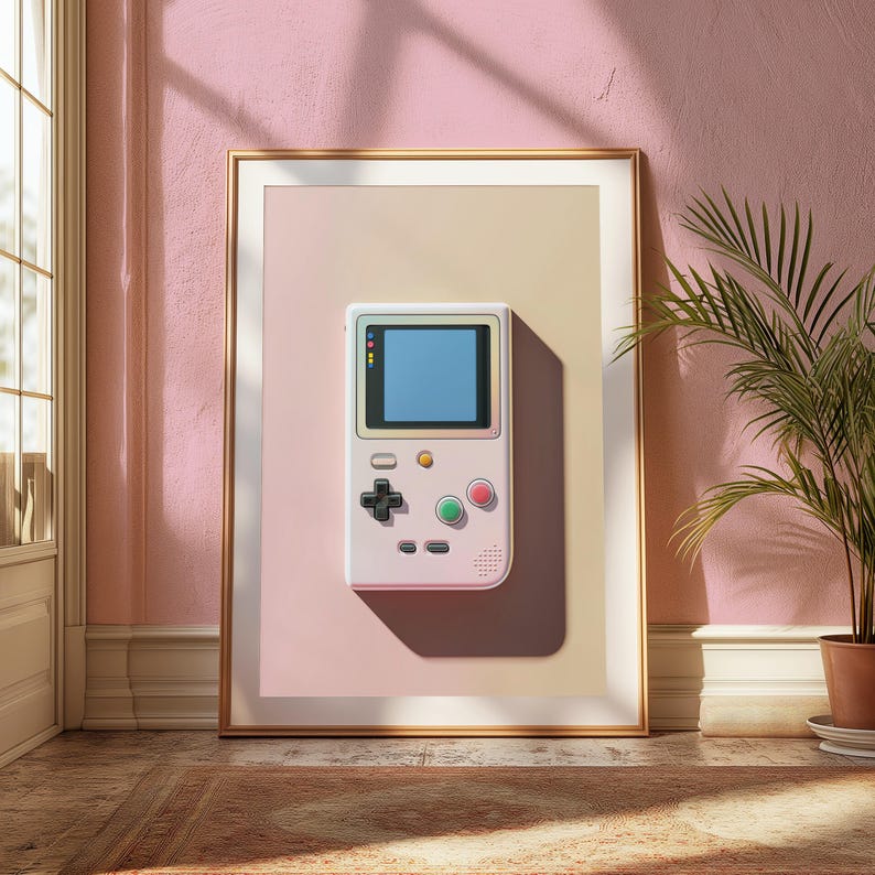May include: A framed wall art print featuring a light pink handheld gaming console with a blue screen, a black directional pad, and green and red circular buttons. The console is centred on a gradient background transitioning from pink to beige.