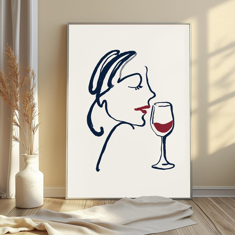 May include: A framed wall art print featuring a continuous dark blue line drawing of a profile of a face with red lips, positioned next to a dark blue line drawing of a wine glass filled with red liquid, set against a plain white background.