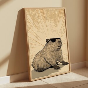 May include: A framed wall art print featuring a detailed illustration of a capybara wearing black sunglasses. The capybara is rendered in shades of brown and tan, set against a light beige background with radiating lines and a subtle dot pattern.