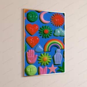 May include: A framed wall art print featuring a vibrant blue background covered in a repeating pattern of glossy, raised-style icons including green faces, red hearts, a pink crescent moon, a red sun, a rainbow, flowers, a hand, and a star.