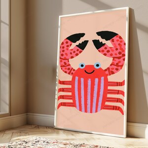 May include: A framed wall art print featuring a stylized crab illustration on a light peach background. The crab has a bright red body with vertical lavender stripes, large pink and red spotted claws with black tips, and eight thin red legs.