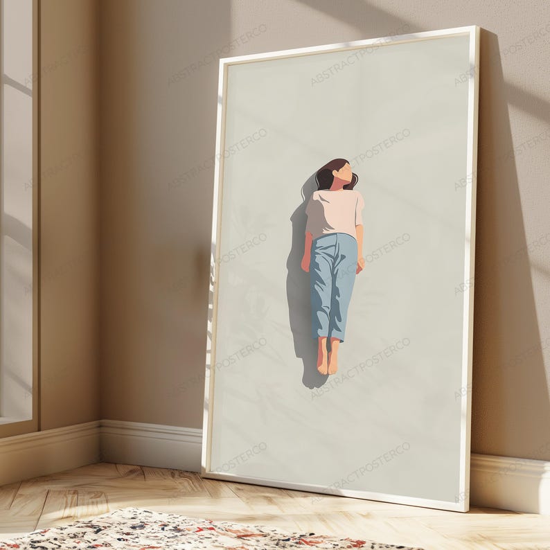 May include: A framed vertical wall art print featuring a minimalist illustration of a person lying down on a light beige background. The person wears a light pink short-sleeved shirt and light blue trousers, casting a dark shadow on the surface.