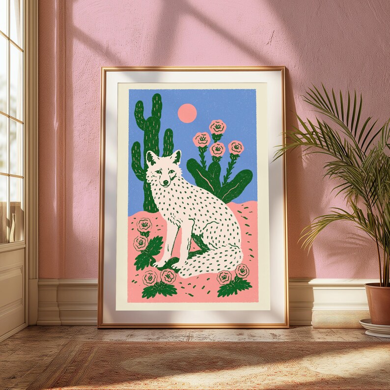 Pu&ograve; includere: Una stampa artistica incorniciata che raffigura una volpe bianca con macchie nere seduta in un paesaggio desertico. La scena include un alto cactus verde, fiori rosa e un piccolo sole rosa su un cielo blu, il tutto in una cornice dorata.