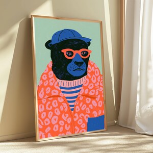 May include: A framed art print featuring a black bear wearing a blue baseball cap, bright orange glasses, and a vibrant orange jacket with a pink leopard print pattern over a blue and pink striped shirt, set against a light green background.