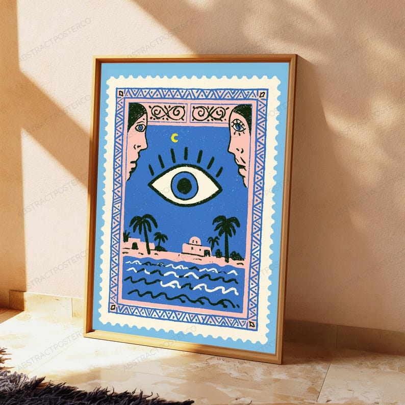 May include: A rectangular art print in a wooden frame featuring a blue postage stamp design. The illustration shows a large central eye, a crescent moon, two faces in profile, palm trees, a building, and wavy water lines in black and pink.